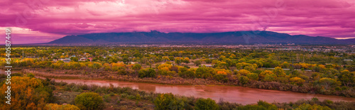 Rio Grand River, autumn landscape with colorful cottonwood trees, and dramatic pink stormy clouds at sunset over Albuquerque city skyline, New Mexico, USA