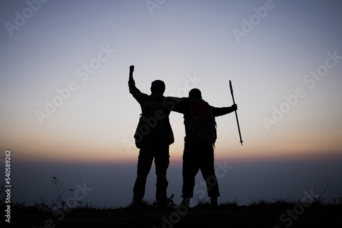 Silhouette of cheering hiking men open arms to the sunrise stand on mountain