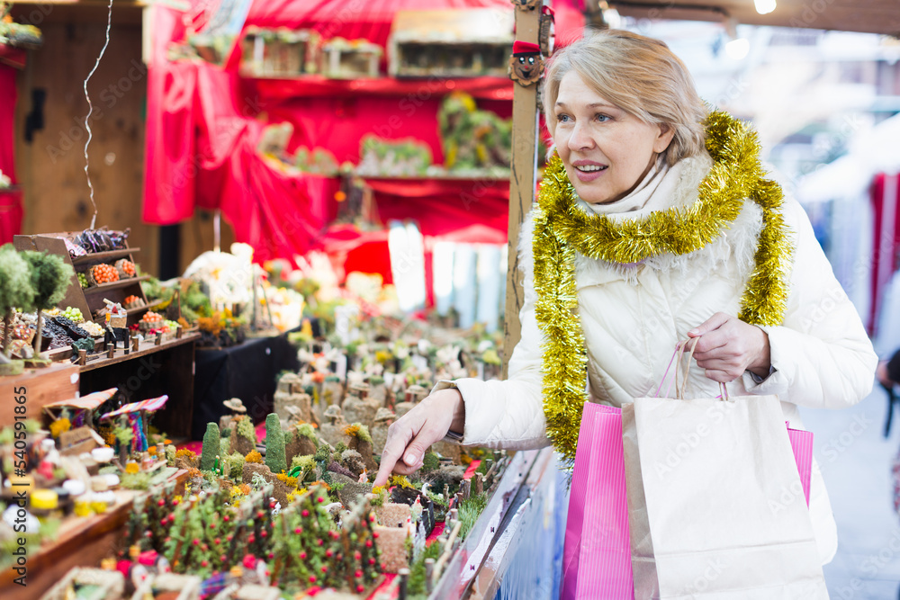 Mature woman choosing decorations at Christmas market and walking