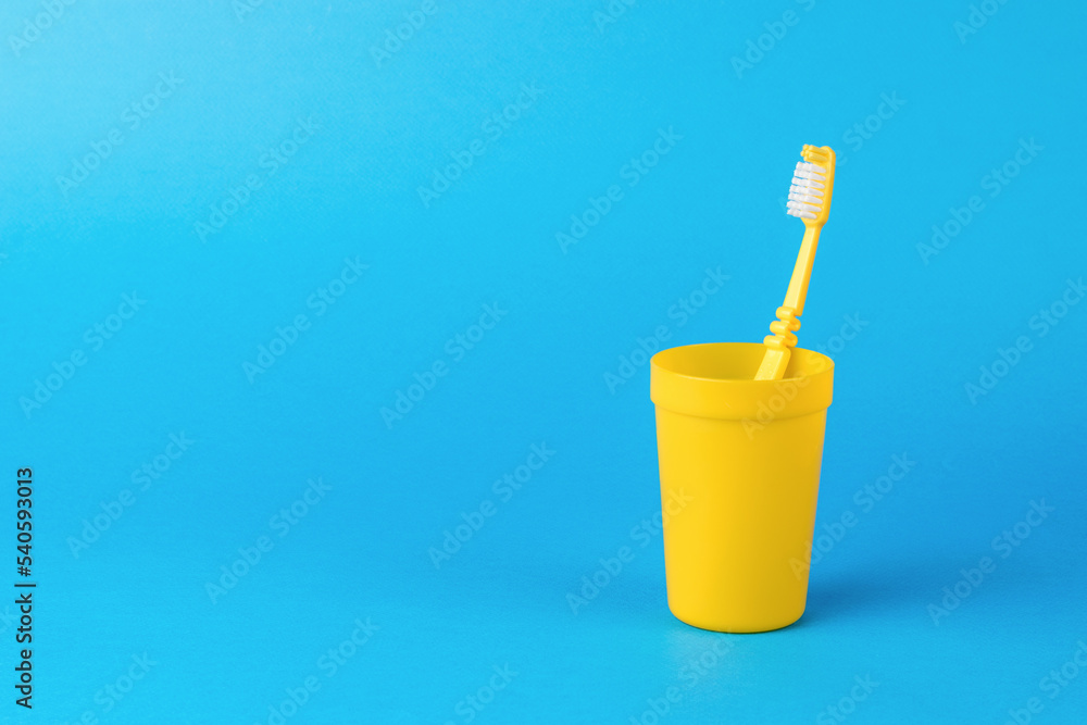 A yellow plastic cup with a yellow toothbrush on a blue background. A yellow plastic cup with a yellow toothbrush on a blue background.