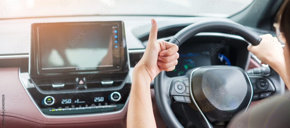 woman hand Thumb up during driving a car on the road, hand controlling steering wheel in electric modern automobile. Journey, trip and safety Transportation concepts