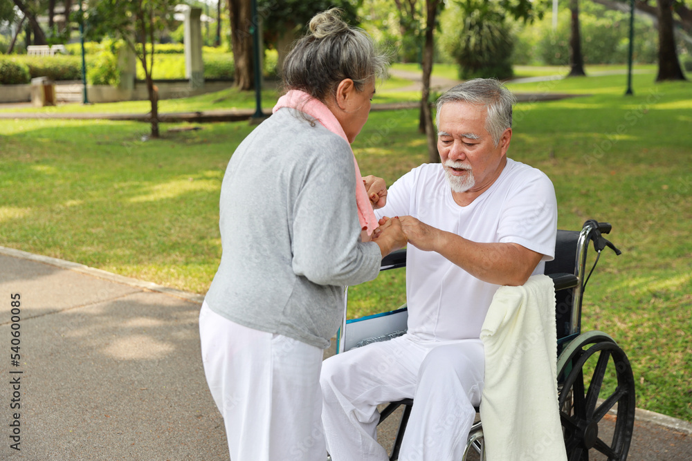 Asian senior woman or caregiver helping and consoling senior man walk with wheelchair at park outdoor. Elderly wife taking good help care and support of elder husband patient outside the house. Asian senior woman or caregiver helping and consoling senior man walk with wheelchair at park outdoor. Elderly wife taking good help care and support of elder husband patient outside the house.