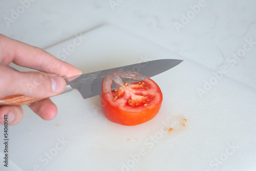 A sharp handcrafted Japanese Knife , slicing cleanly through a fresh tomato and other vegetables, skilled chef