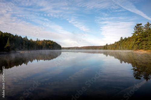 Reflections of a sky filled with clouds and a tree lined lake on a calm day in autumn. Head Lake, Algonquin Provincial Park, Ontario, Canada.