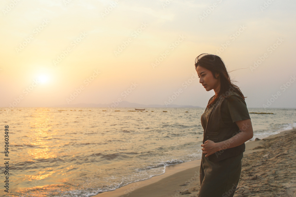 A young woman wearing a green dress stands in the sea at the beach enjoying the early summer morning sunrise view.
