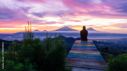 silhouette of A man is sitting in a park with a view of the sunrise and a row of mountains - Mangli sky view, Indonesia