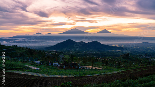 Beautiful reddish orange sunrise sky with mountain range and plantation on the foreground - View from slope of Sumbing Mountain