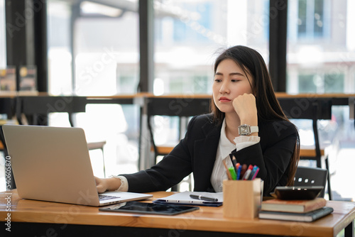 Asian businesswoman thinking, seriously and working with a laptop on the wooden table in the cafe.