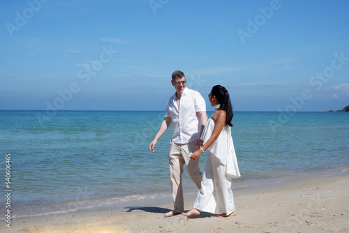 A man and woman walk hand in hand on the beach. bright blue sea.