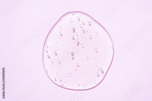 Drop of transparent cosmetic gel or liquid with bubbles over pink background. Drop of face cosmetic serum. Selective focus