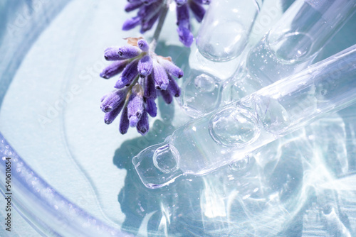 Pipette with cosmetic liquid or face serum with lavender flowers over blue background. Texture of hydrolate or cosmetic oil with lavender extract for skin care. Selective focus photo