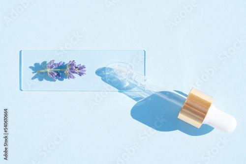 Pipette with cosmetic lavender oil over blue background. Texture of hydrolate or cosmetic oil with lavender extract for skin care. Selective focus photo