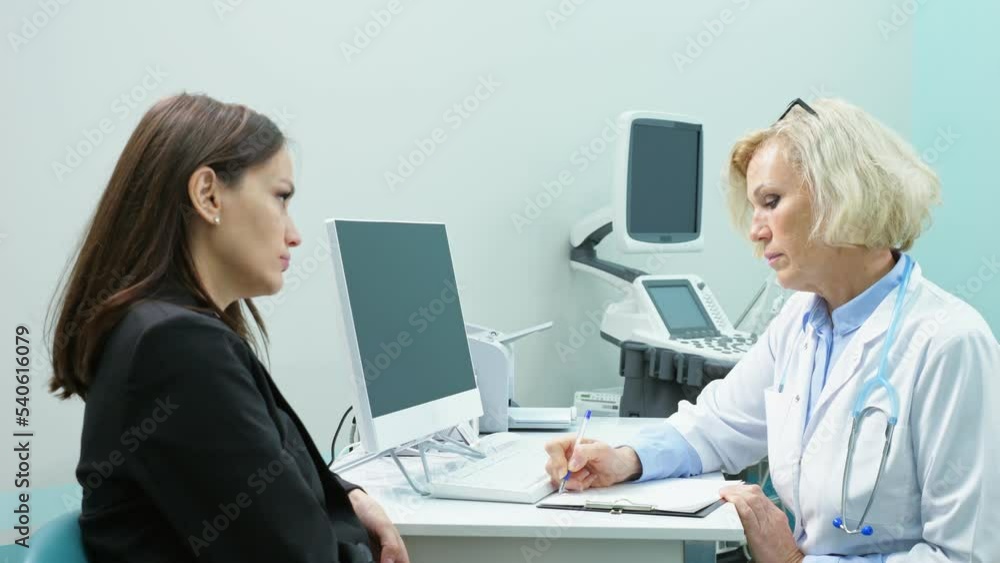 Mature blonde doctor writes down complaints in patient checklist form. Young woman describes complications to respiratory system after taking heavy antibiotics Mature blonde doctor writes down complaints in patient checklist form. Young woman describes complications to respiratory system after taking heavy antibiotics