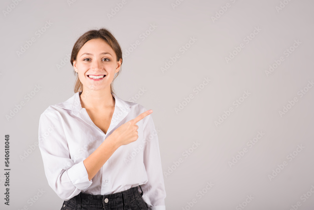 A businesswoman in a white shirt points her finger at a copy space for advertising on a gray background. A businesswoman in a white shirt points her finger at a copy space for advertising on a gray background.