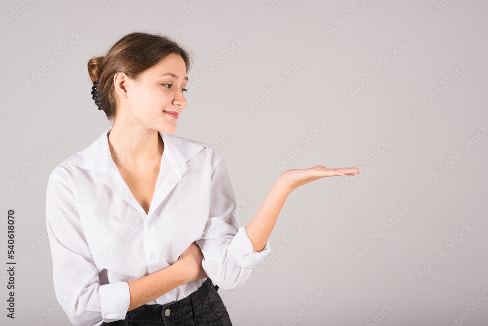 A businesswoman presents a product in the palm of her hand with a copy space for advertising on a gray background. A businesswoman presents a product in the palm of her hand with a copy space for advertising on a gray background.