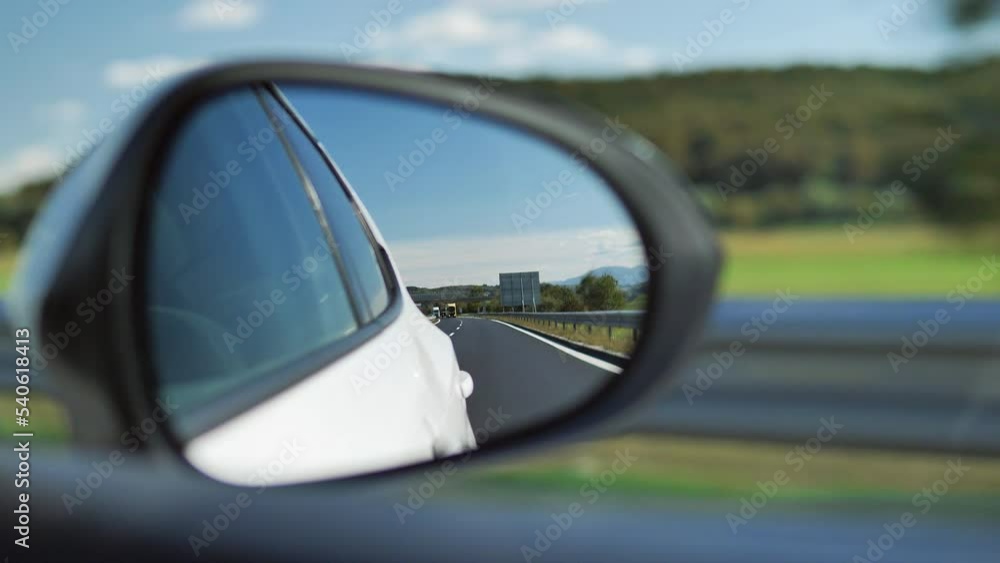 Side mirror of a white car. Focus on the backside of the road. Side mirror of a white car. Focus on the backside of the road.