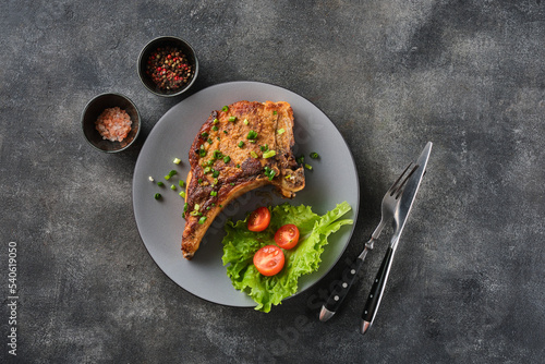 Grilled pork chop on grey plate sprinkled with green onions with salad and cherry tomatoes.
