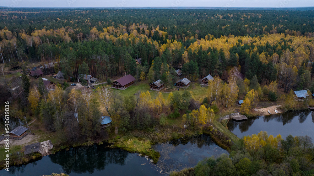 Fototapeta premium panoramic view from a drone on the edge of the forest with wooden houses and a river against the backdrop of autumn nature