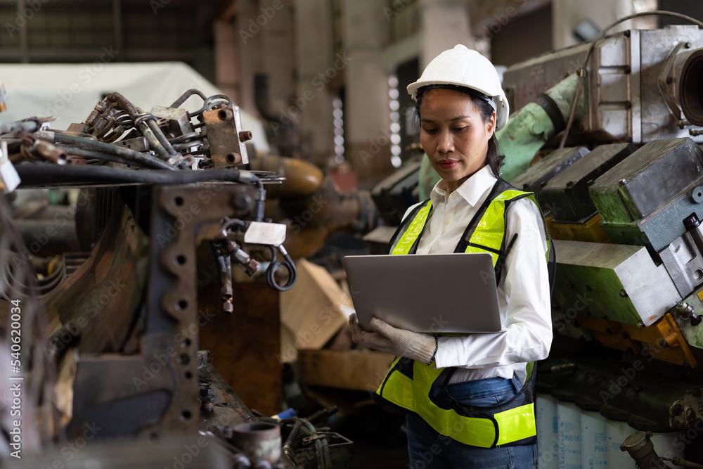 Asian female engineer worker working with laptop computer checking, maintaining machinery, mechanical machine at the industry factory. Asian woman technician wear safety uniform working in the factory Asian female engineer worker working with laptop computer checking, maintaining machinery, mechanical machine at the industry factory. Asian woman technician wear safety uniform working in the factory