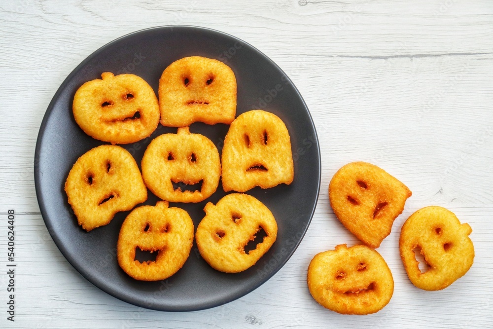 Fried halloween potato shapes on black plate with white wood background.Creative art food idea for kids halloween party.Top view.Copy space Fried halloween potato shapes on black plate with white wood background.Creative art food idea for kids halloween party.Top view.Copy space