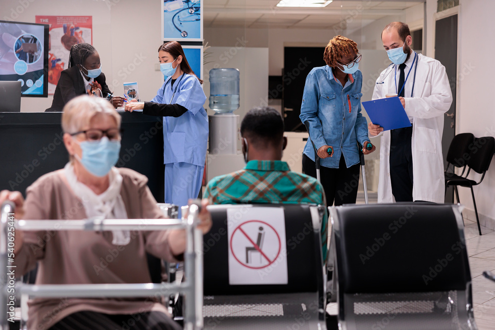 Fototapeta premium African american patient in crutches at hospital lobby, talking to male doctor about healthcare and recovery. Woman with chronic disability and impairment doing on toutine checkup visit.