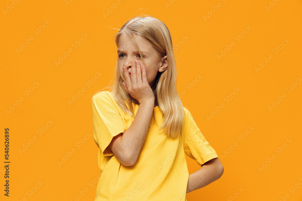 a cute, thoughtful girl stands on a yellow background in a yellow T-shirt with a very puzzled face. Horizontal studio photography with space to insert advertising mockup a cute, thoughtful girl stands on a yellow background in a yellow T-shirt with a very puzzled face. Horizontal studio photography with space to insert advertising mockup
