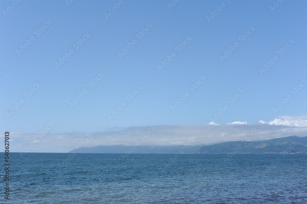 Picturesque seashore with beach and ocean waves and horizon on a sunny day with clear blue sky and calm ocean in Hokkaido, northern Japan, Asia Picturesque seashore with beach and ocean waves and horizon on a sunny day with clear blue sky and calm ocean in Hokkaido, northern Japan, Asia
