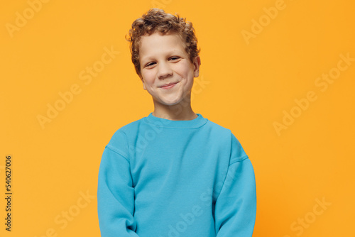 portrait of a cute, pleasant boy with curly hair in a blue sweater on a yellow background, pleasantly smiling at the camera