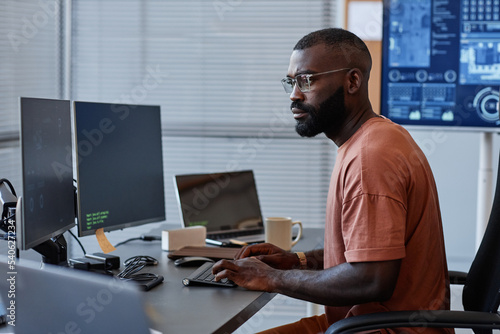 Side view of black software engineer using computer in high technology office, data systems and programming