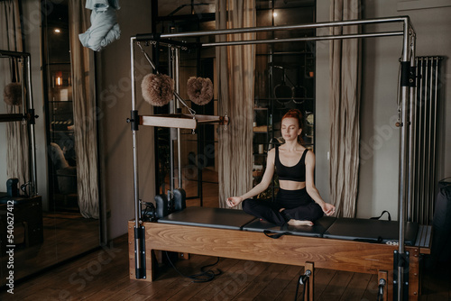 Young fit woman sitting in lotus position on trapeze table