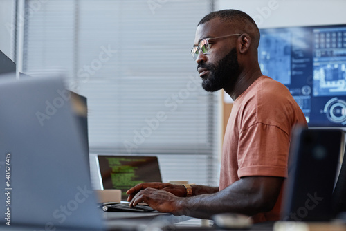 Side view portrait of black software developer using computer in high technology office, data systems and programming