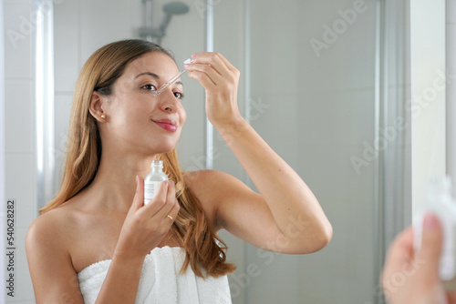 Beauty woman applying hyaluronic acid on the face in the bathroom. Skin care routine. photo