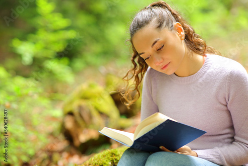 Woman reading a paper book sitting in nature #540628497
