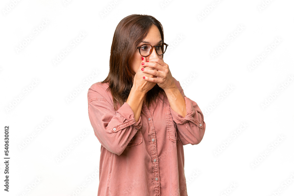 Middle-aged caucasian woman over isolated background covering mouth and looking to the side Middle-aged caucasian woman over isolated background covering mouth and looking to the side