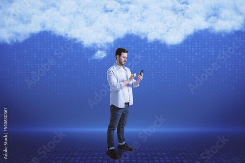 Attractive young european businessman with smartphone on blurry digital blue background with abstract cloud. Cloud computing  big data and digital transformation concept.