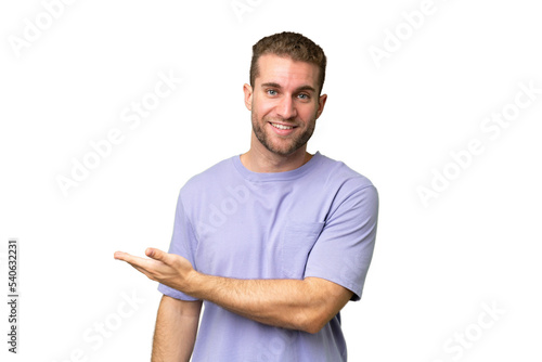 Young handsome caucasian man isolated on green chroma background presenting an idea while looking smiling towards