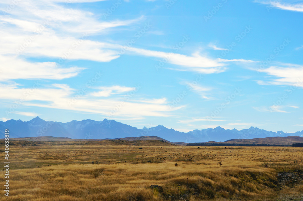 Scenic blue shaded mountain range and dry farmland under bright blue autumn sky.