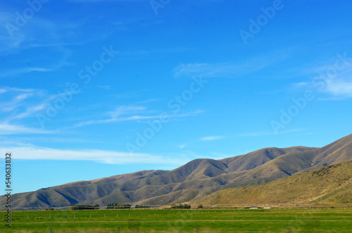 Scenic blue shaded mountain range and dry farmland under bright blue autumn sky.