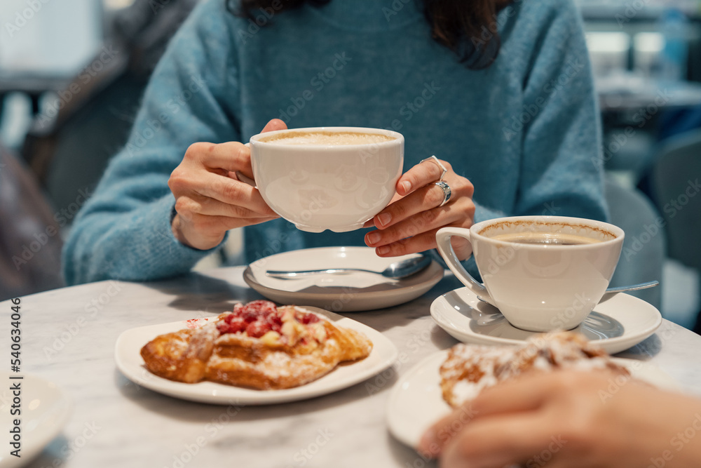 Woman drinking coffee from white cup in the cafe. Delicious breakfat with almond croiisant and coffee Woman drinking coffee from white cup in the cafe. Delicious breakfat with almond croiisant and coffee