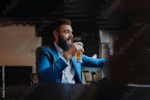 Young adult stylish man with a beard holding a pint glass of beer smiling