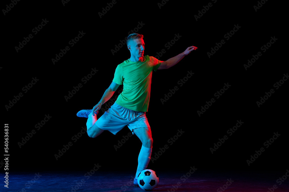 Goal. Young soccer, football player in motion and action with ball isolated on dark background in neon light. Concept of achievement, creativity, sport, energy, championship Goal. Young soccer, football player in motion and action with ball isolated on dark background in neon light. Concept of achievement, creativity, sport, energy, championship