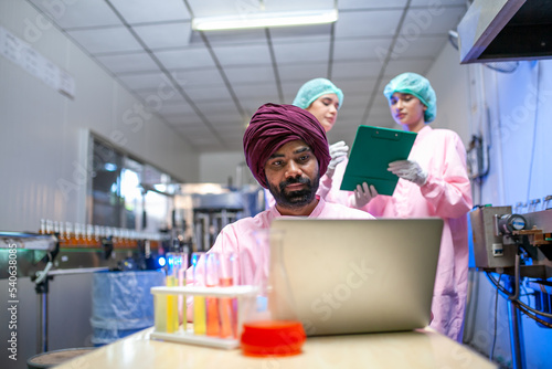 Asian scientists use test tube checking juice product on the production line in the beverage factory. Manufacturer checks quality of food industry.