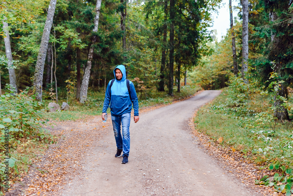 Fototapeta premium A middle age male hiking with a backpack.Man walks along the autumn forest path way.A healthy lifestyle in nature.