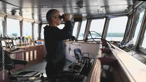 Deck officer with binoculars on navigational bridge. Seaman on board of vessel. Commercial shipping.  photo