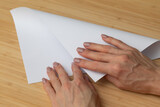 A woman with a beautiful manicure folds a sheet of white paper. A writing blank. A white piece of paper in a woman's hands.
