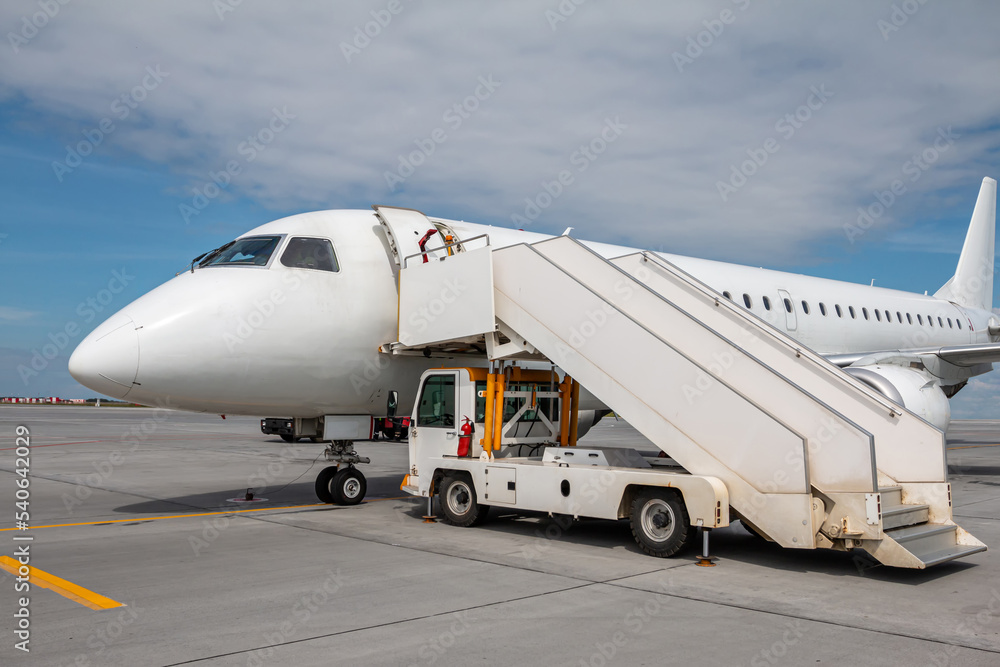 White passenger airliner with a boarding steps on the airport apron White passenger airliner with a boarding steps on the airport apron