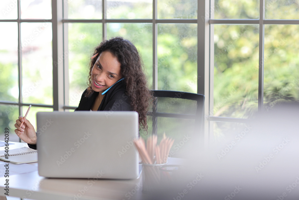 Attractive professional latin female employee worker sitting, using laptop computer with paperwork at home workplace. Businesswoman using smart mobile phone while holding credit card. Attractive professional latin female employee worker sitting, using laptop computer with paperwork at home workplace. Businesswoman using smart mobile phone while holding credit card.