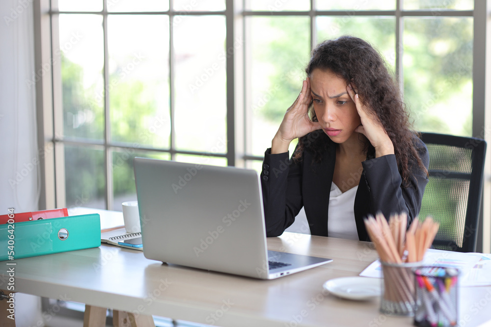 Adult businesswoman sitting and touching her head and looking at computer in office after bad news business failure or get fired and feeling discouraged, distraught and hopeless in modern office Adult businesswoman sitting and touching her head and looking at computer in office after bad news business failure or get fired and feeling discouraged, distraught and hopeless in modern office
