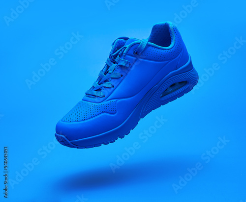 Flying sneaker on blue background. Fashionable stylish leather unisex sports casual shoes. Creative minimalistic footwear layout. Lifestyle product photo, levitation and urban style concept.