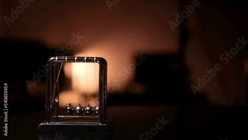 Newton's cradle clattered, back and forth, set on a black table with orange lights behind it. photo